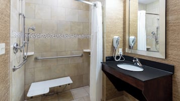 A bathroom with a shower, a sink, a mirror, and a hand dryer.