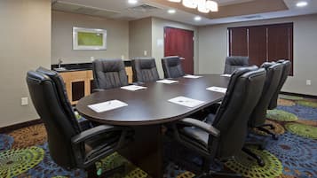 A conference room with a large table, black leather chairs, a small kitchenette, and a patterned carpet.