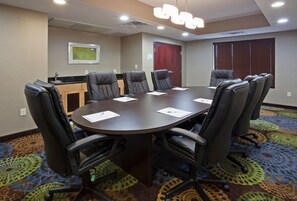 Une salle de conférence dotée d’une grande table, de chaises en cuir noir, d’un petit coin cuisine et d’un tapis à motifs.