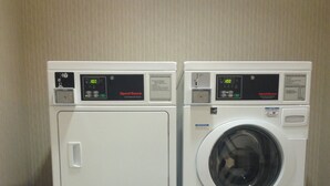 Deux sèche-linge commerciaux superposés dans une buanderie, avec un sol carrelé et une poubelle.