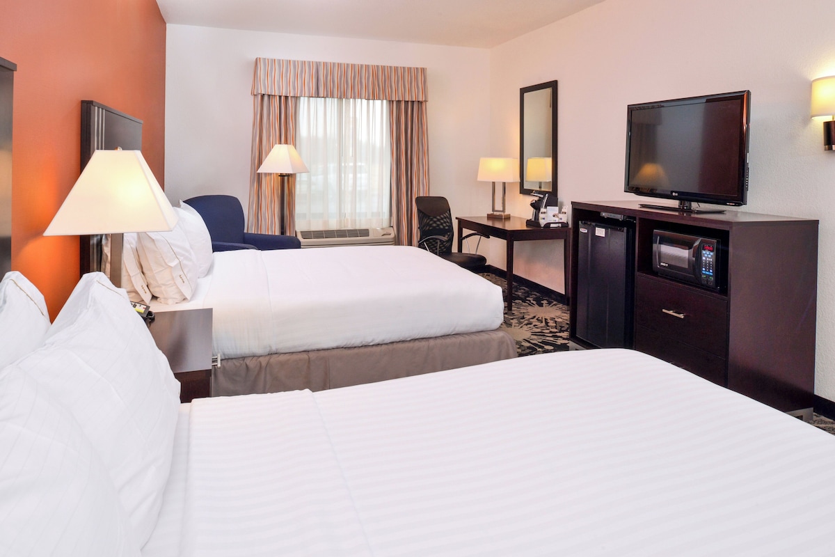 A hotel room with two beds, a desk with a computer, a television, and a minibar.