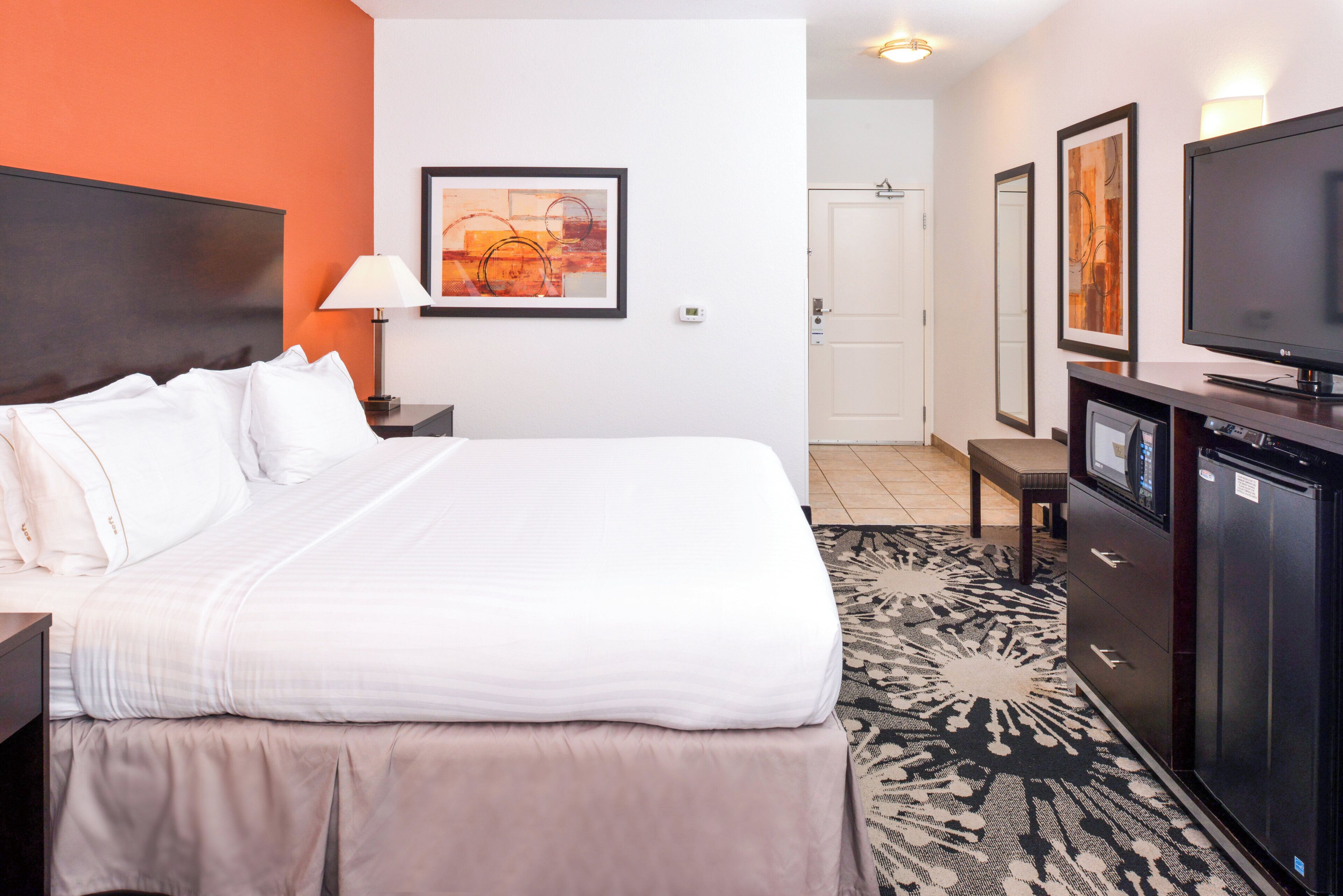 A hotel room with a bed, a desk, a television, and a door.