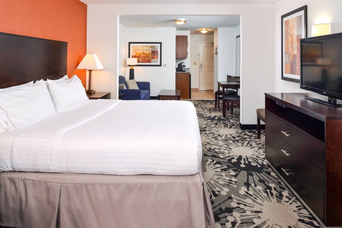 A hotel room with a large bed, a desk, a television, and a dining area.