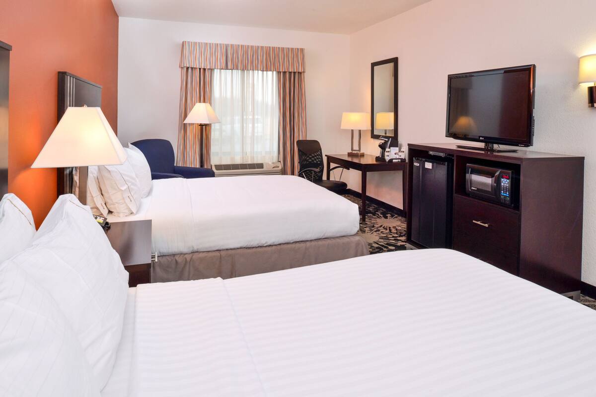 A hotel room with two beds, a desk with a chair, a television, and a minibar.