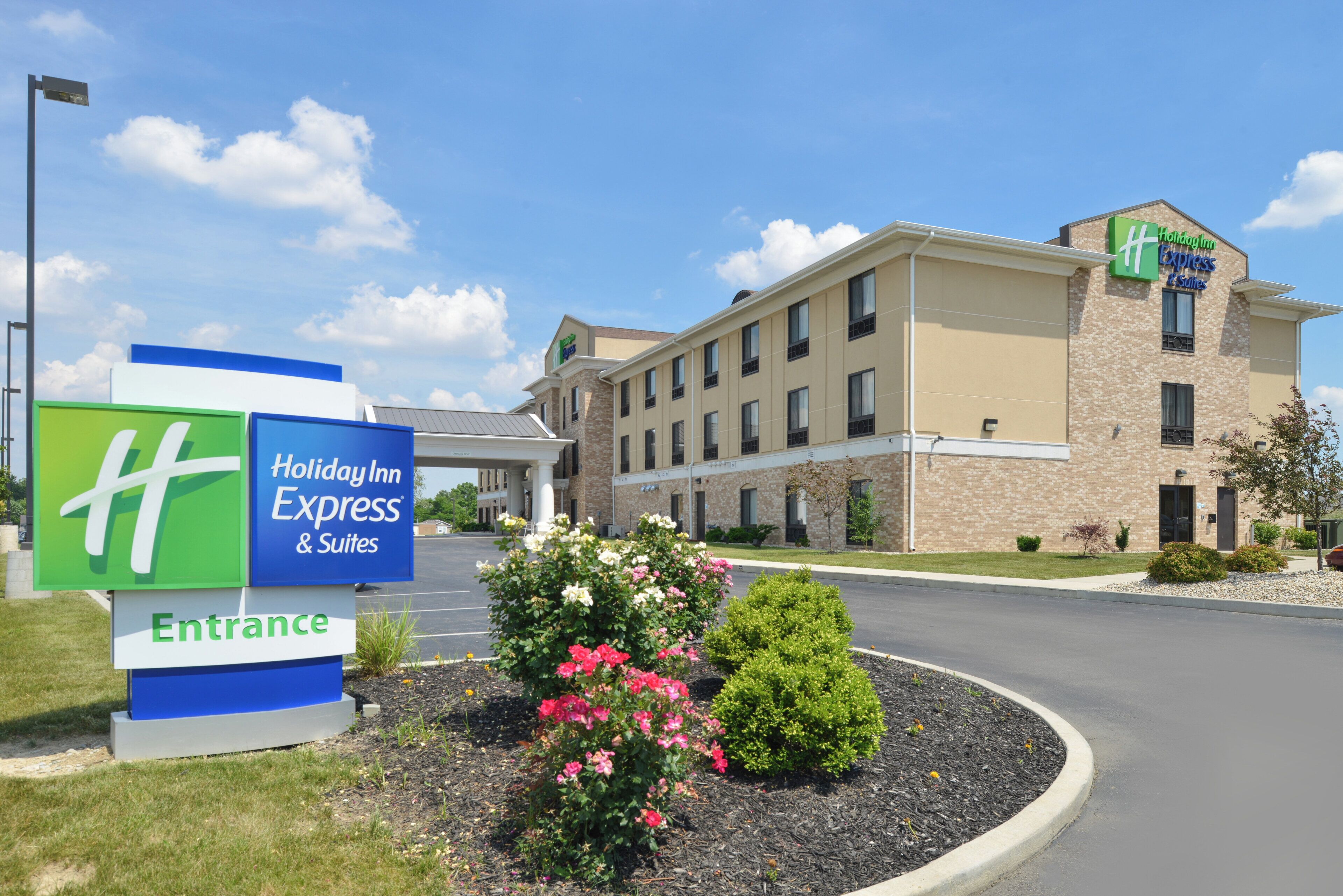 A Holiday Inn Express & Suites building with a clear entrance sign, a parking lot, and a landscaped area with flowers.