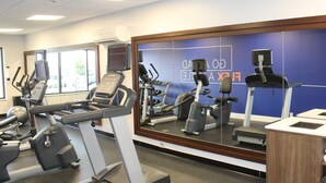 Une salle de sport équipée de divers appareils d’exercice, dotée d’un grand miroir et d’un mur bleu sur lequel est inscrit un texte.