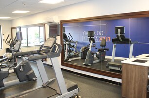 Un gimnasio con equipo de ejercicio variado, un espejo grande y una pared azul con texto.