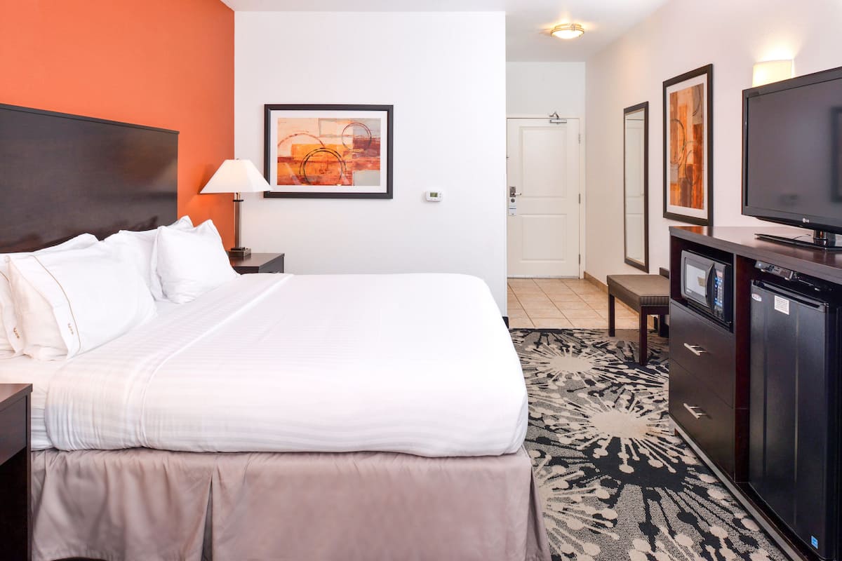 A hotel room with a large bed, a desk, a TV, and artwork on the walls.