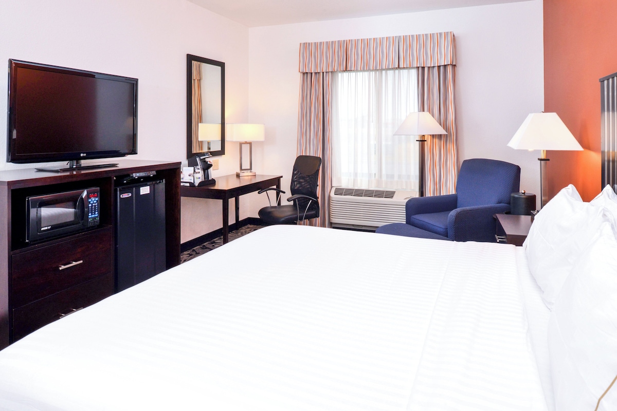 A hotel room with a bed, a desk, a chair, a television, a lamp, and a window with curtains.