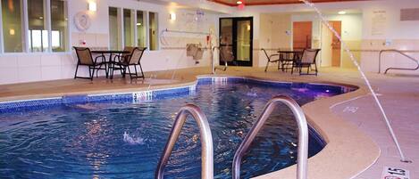 An indoor swimming pool with a diving board, lounge chairs, and a tiled floor.