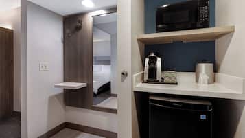 A hotel room with a shower, a bed, a microwave, a coffee machine, and a dishwasher.