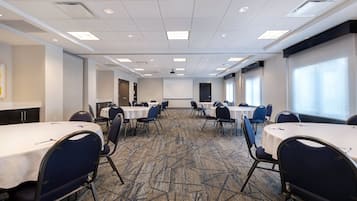 A conference room with multiple tables and chairs, a carpeted floor, and a projector screen.
