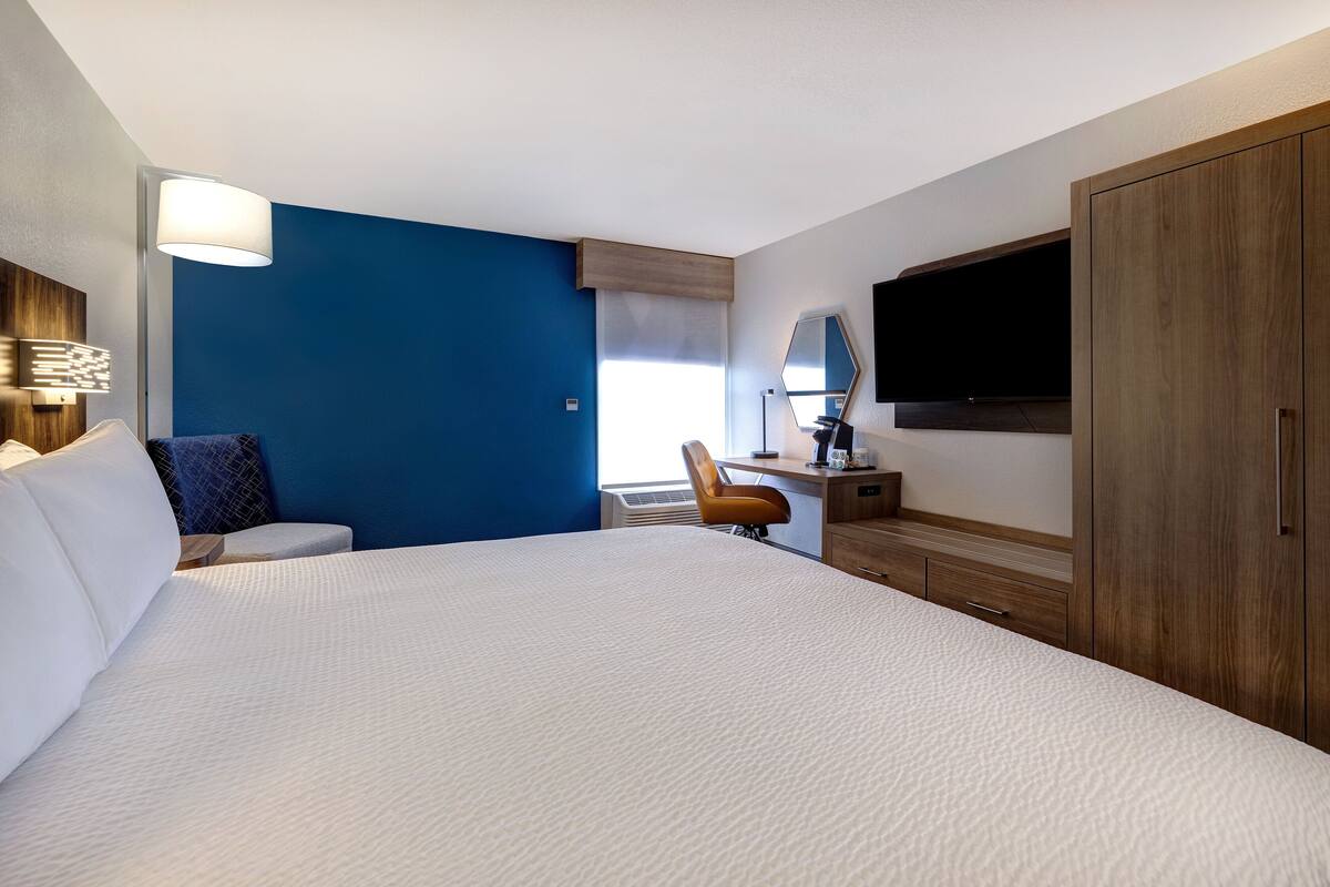 Une chambre d’hôtel avec un grand lit, un bureau avec une chaise, une télévision et une armoire.