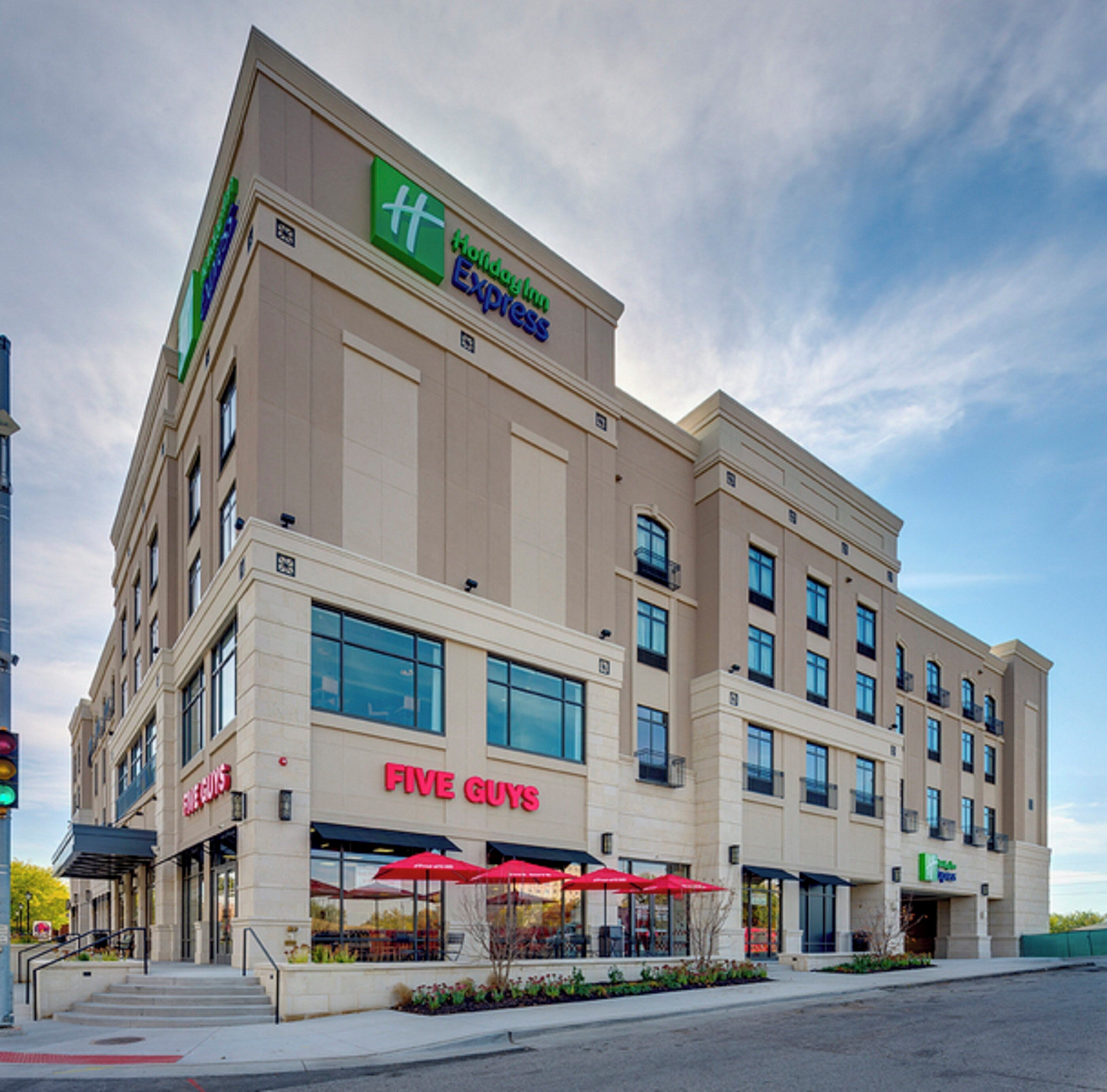 A hotel with a 'Five Guys' restaurant on the ground floor, a 'Holiday Inn Express' sign above, and a clear sky.