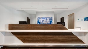Een receptie met een houten balie, een blauwe geometrische wanddecoratie en een bord met daarop ‘inchecken’.