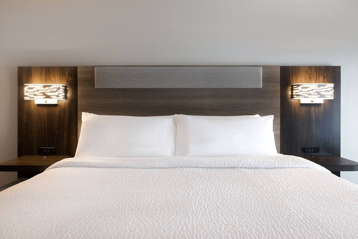 Une chambre d’hôtel avec un grand lit, deux tables de chevet et des luminaires fixés au mur.