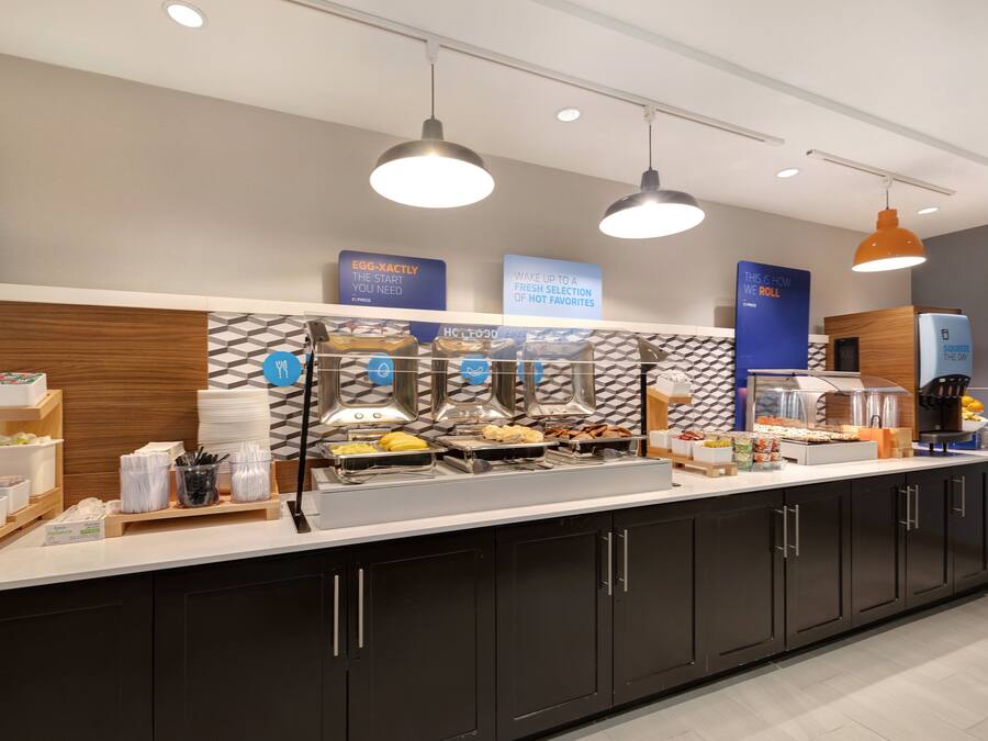 A buffet setup with various food items and utensils, overhead lighting, and informational signs.