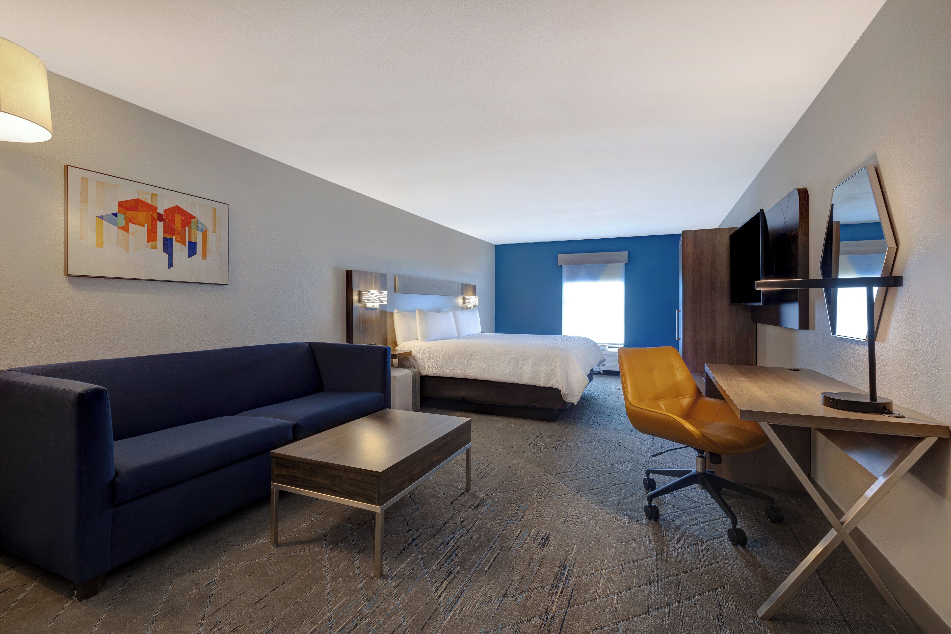 Une chambre d’hôtel avec un lit, un canapé, un bureau, une chaise, une télévision et un tableau au mur.