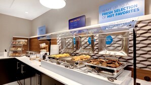 Ein reichhaltiges Buffet mit verschiedenen Speisen und einem Schild, das frische Frühstücksmöglichkeiten bewirbt.