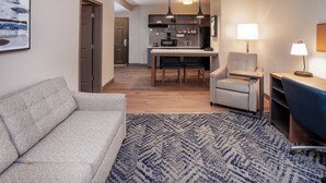 Una sala moderna con un sofá, una alfombra estampada, una zona de comedor con mesa y sillas, y una cocina al fondo.