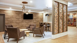 Un moderno vestíbulo con piso de madera, una zona de estar con sofás y una mesa redonda, un televisor montado en la pared y un separador de madera con un diseño geométrico.