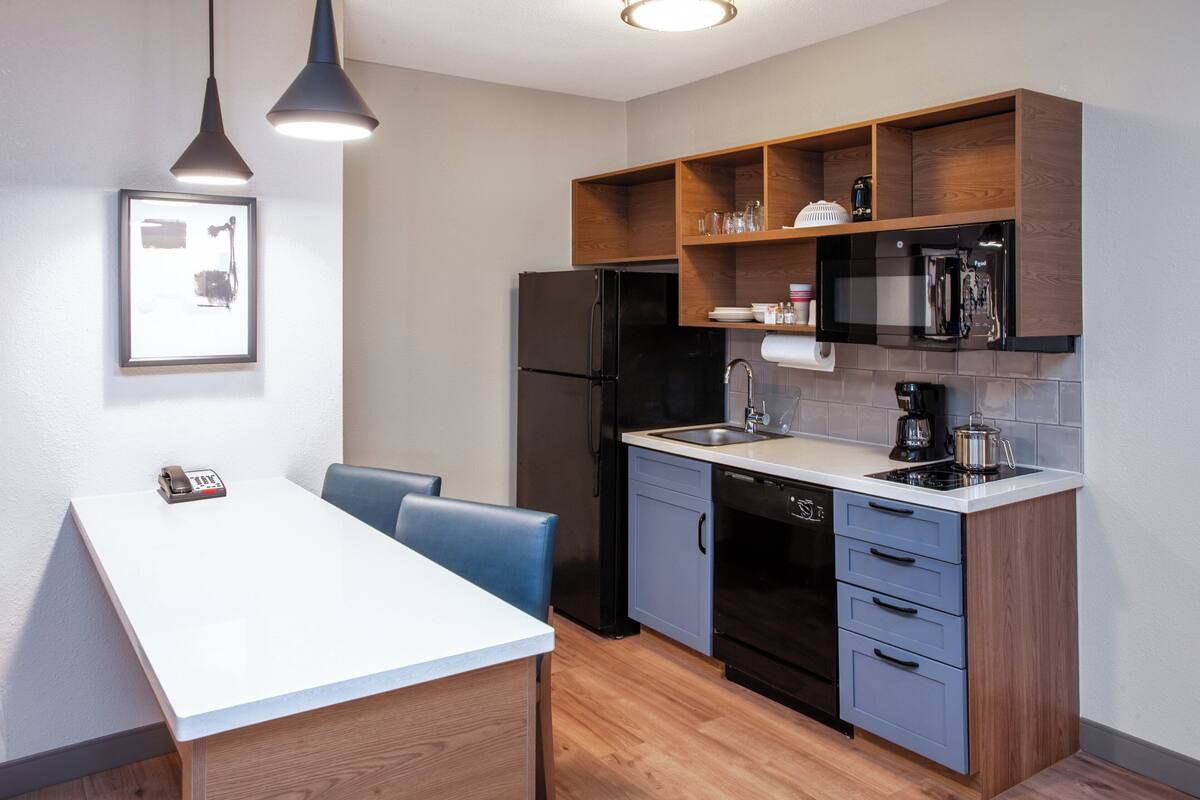 A compact kitchen with a white countertop, black appliances, and wooden shelves.