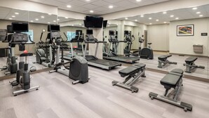 Un gimnasio con diferentes equipos de ejercicio, espejos y un televisor en la pared.