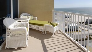 Een balkon met wit rieten meubilair, een groene tafel en uitzicht op de oceaan.
