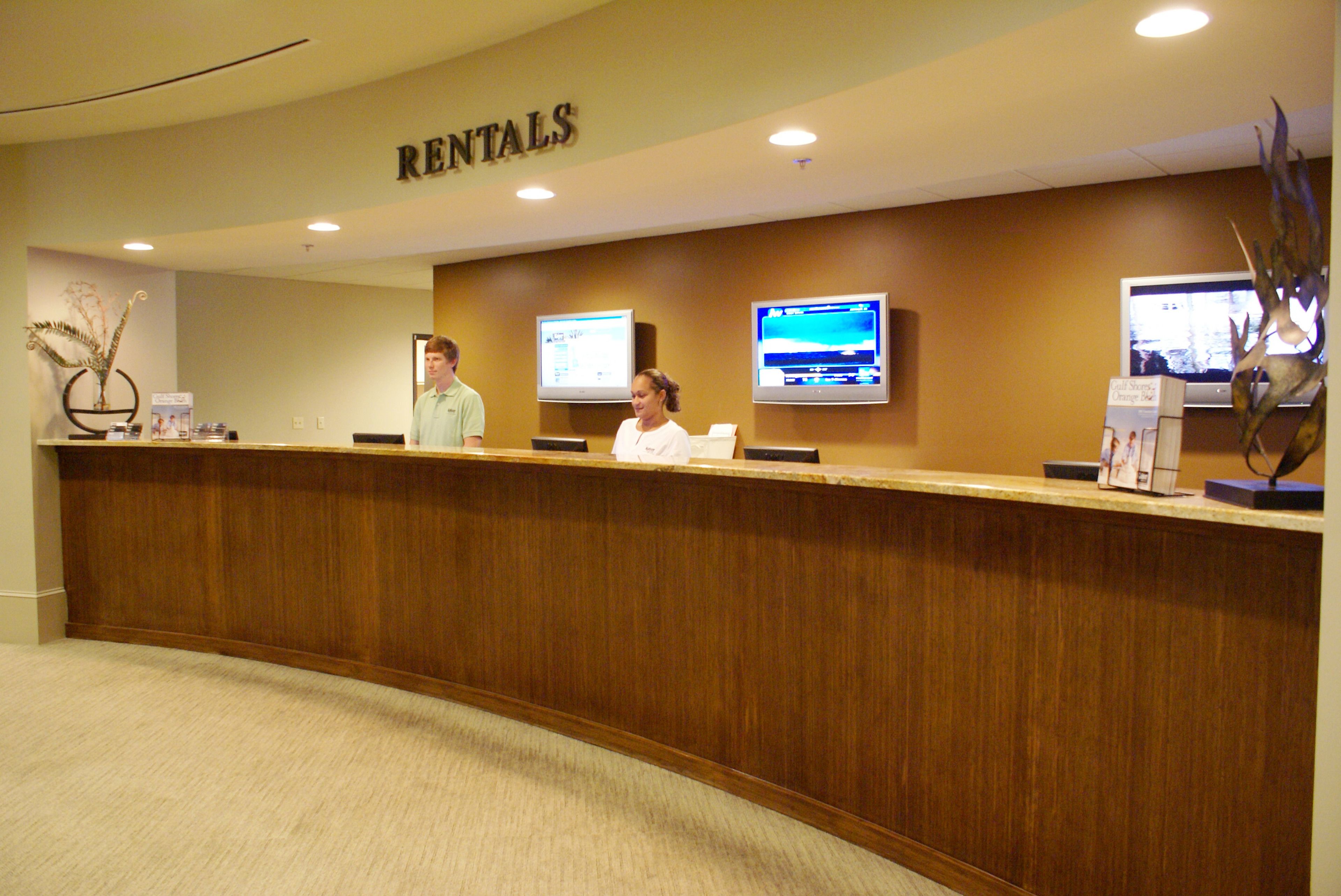 A reception desk with a 'RENTALS' sign above, two monitors, and a decorative plant.