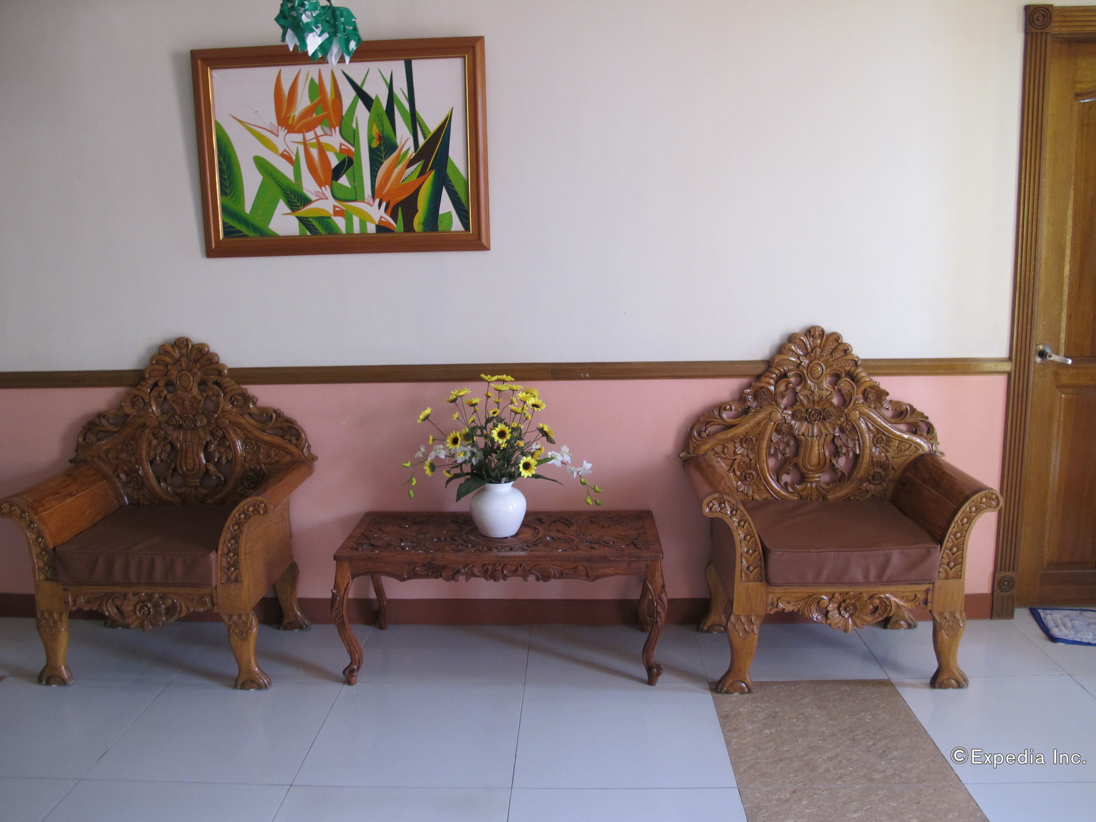 A room with two ornate wooden chairs, a small table with a vase of flowers, and a framed botanical painting on the wall.
