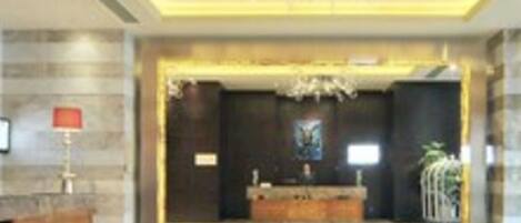 Un vestíbulo con piso de mármol, una recepción, una araña y una obra de arte enmarcada en la pared.