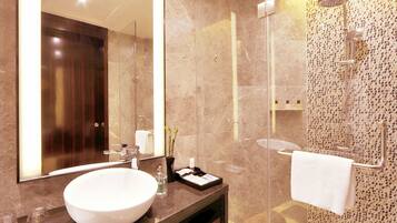 A modern bathroom with a large mirror, a round sink, a glass shower enclosure, and a marble-tiled floor.