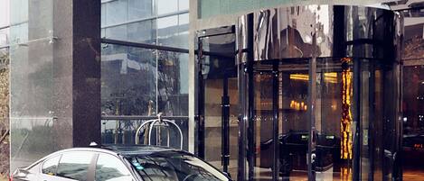 A black car parked in front of a building with a glass facade and a sign with Chinese characters.