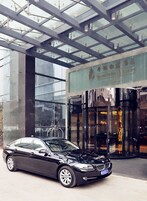A black car parked in front of a building with a glass facade and a sign with Chinese characters.