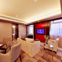 Una habitación de hotel moderna con sofá, sillones, una mesita de café y una pantalla de televisión.