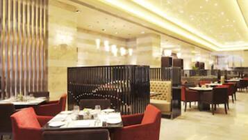 A modern restaurant with a high ceiling, warm lighting, and a mix of seating arrangements including tables and booths.