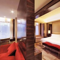 Habitación de hotel con una cama grande, un sofá rojo y vistas a la ciudad desde la ventana.