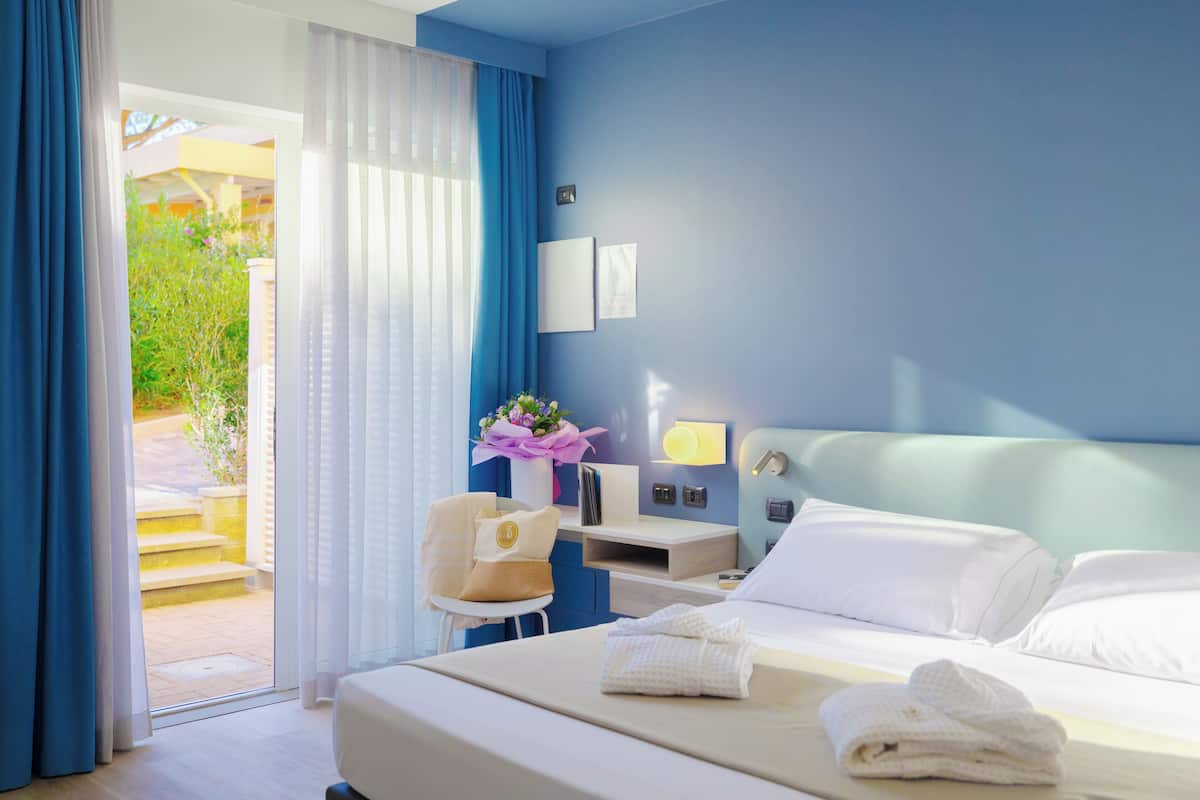 A hotel room with a bed, a desk, a chair, and a view of the outside.
