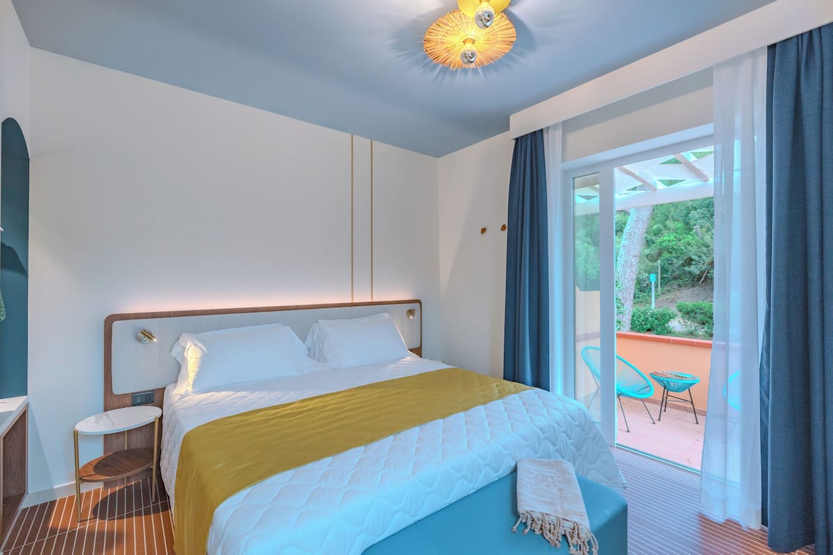 A hotel room with a bed, a small table, a chair, and a view of the outdoors.
