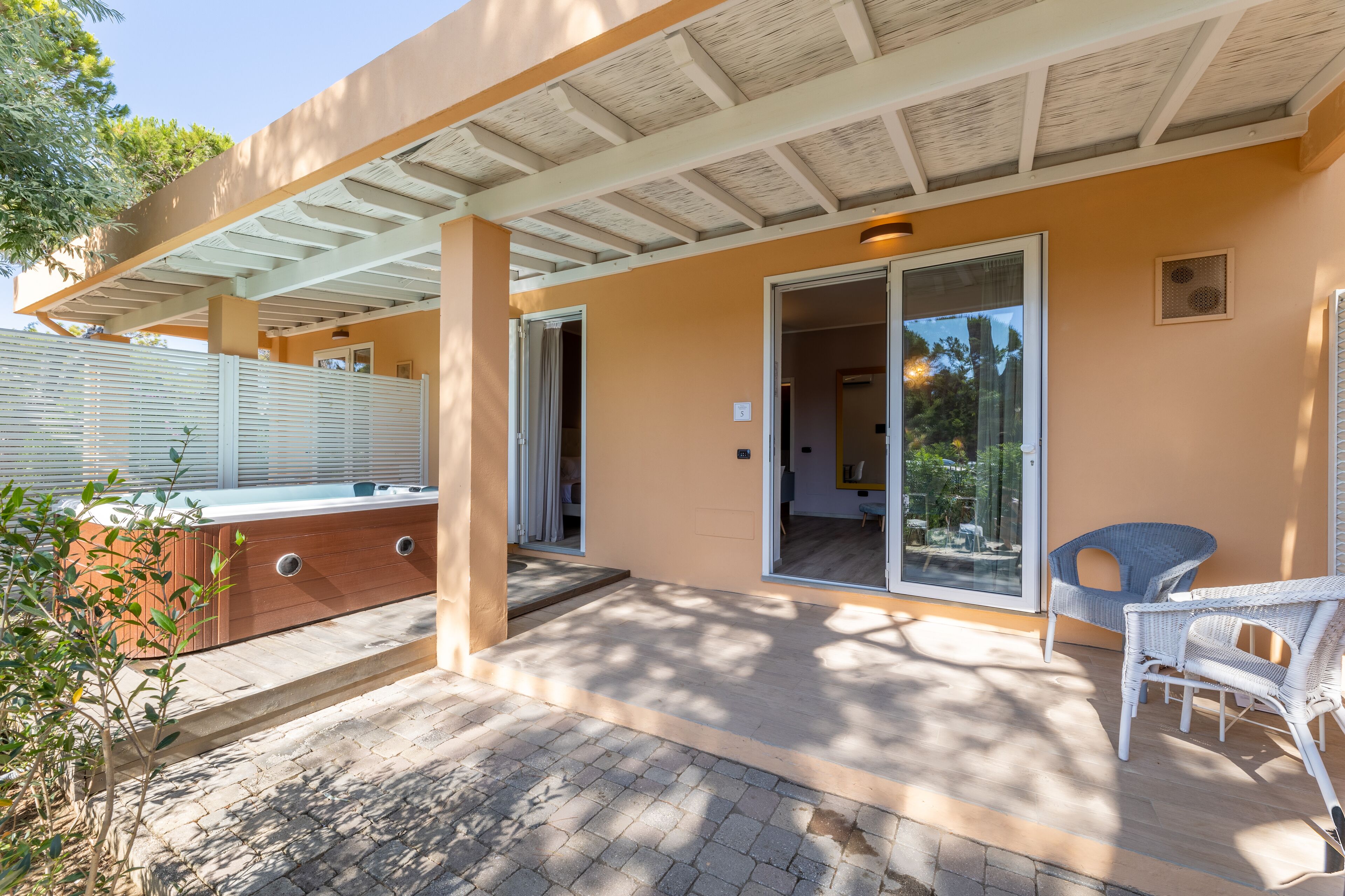 A covered patio with a hot tub, wicker chairs, and a sliding glass door leading to an interior room.