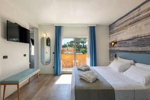 A modern hotel room with a bed, a bench, a TV, and a balcony with a view of the outdoors.