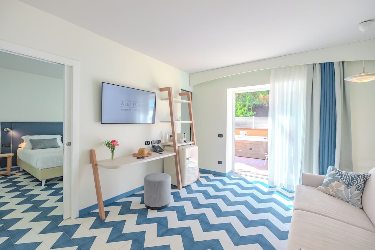 A modern room with a chevron-patterned floor, a bed, a desk with a chair, a ladder, and a sofa.