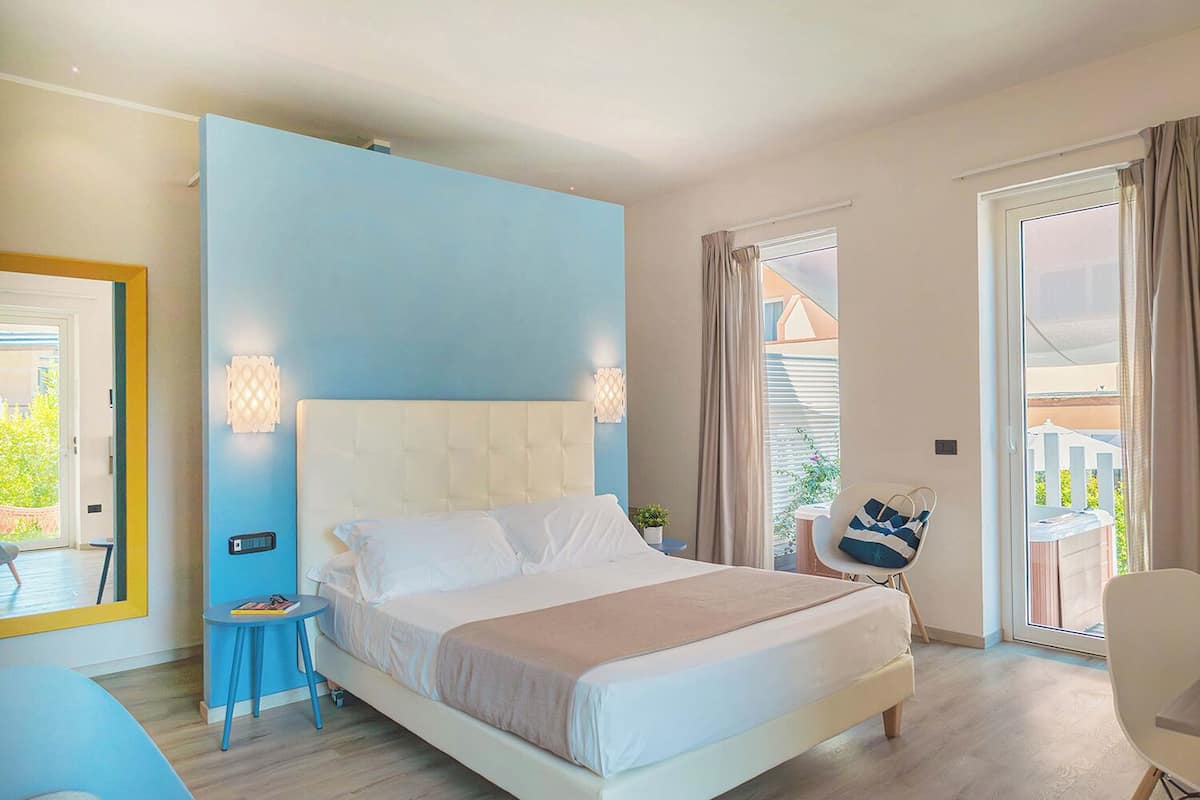 A bedroom with a bed, a bedside table, a chair, a window, and a balcony.