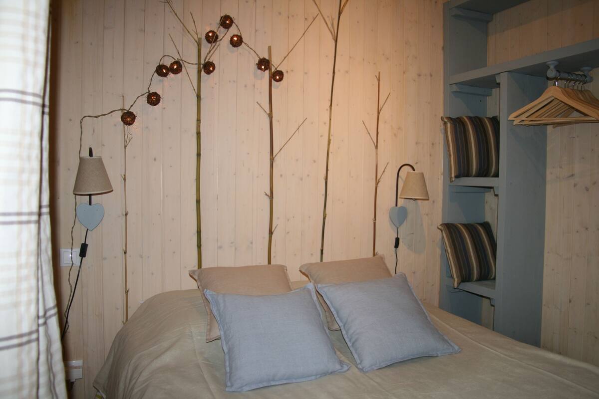 Un dormitorio con cama, dos almohadas, lámpara colgante y armario con cortinas a rayas.