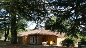 Una cabaña de madera con techo de tejas, una hamaca y una mesa dispuesta en el exterior.