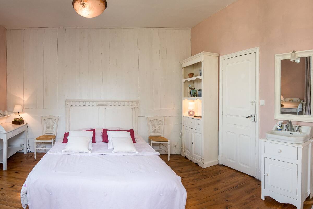 Un dormitorio con cama, escritorio, silla, armario y baño con lavabo y espejo.
