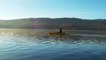 A calm lake with a person fishing from a yellow kayak.