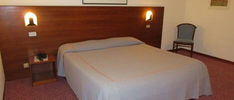 A hotel room with a bed, a nightstand with a phone, a chair, and two wall-mounted lights.