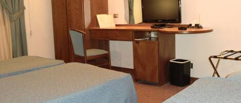 A hotel room with two single beds, a wooden desk with a television, a chair, and a small trash bin.