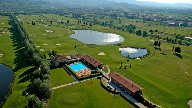 An aerial view of a golf course with a swimming pool, a clubhouse, and a lake. - Hotel Giardino (Prato)